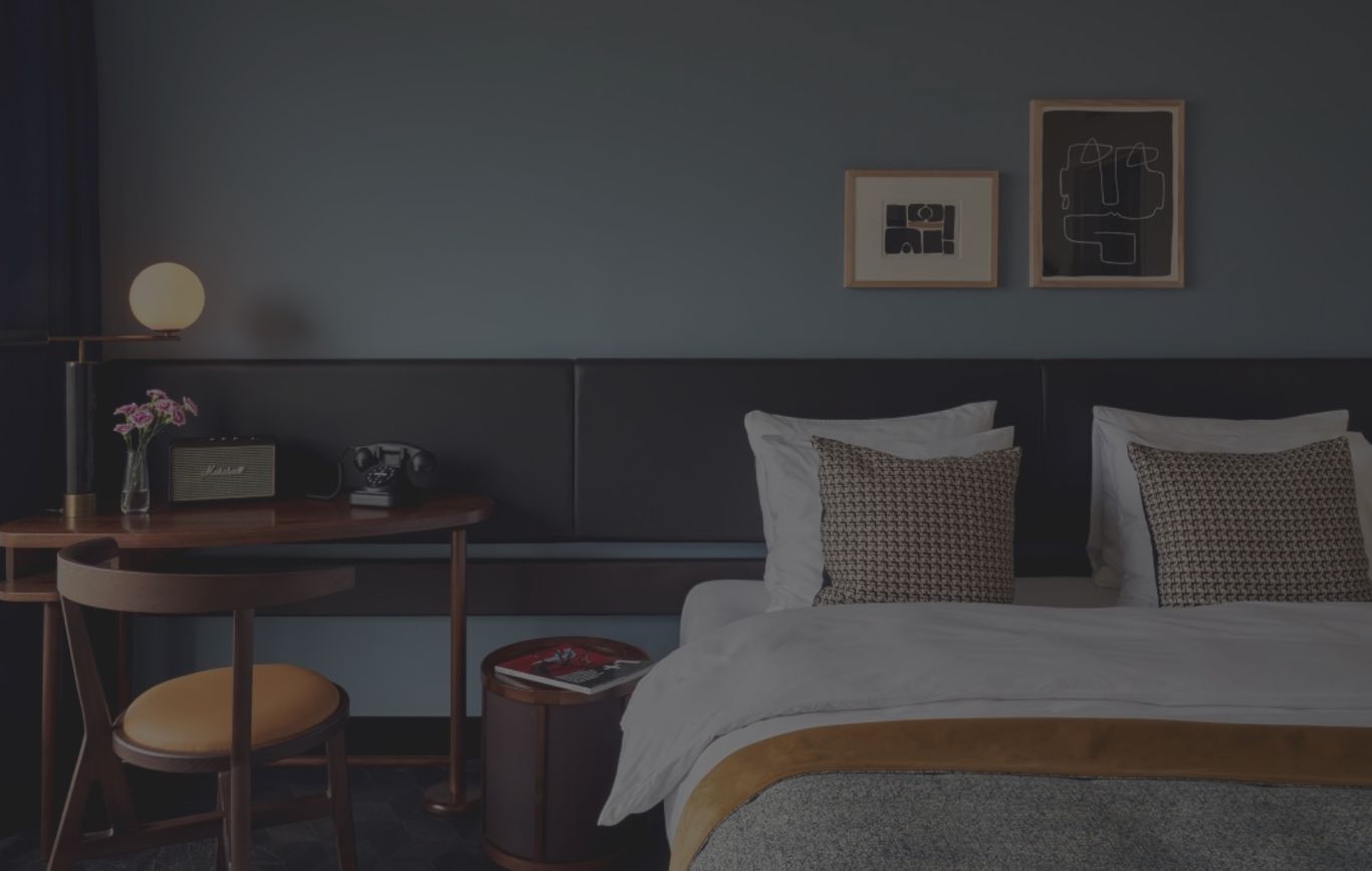 Hotel interior with bedroom, a bed and desk infront of a blue wall